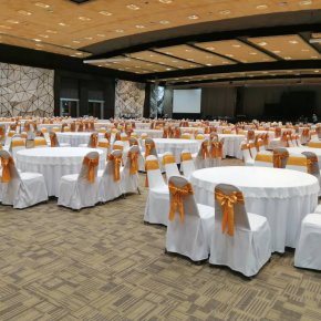 โต๊ะจัดงานกลมพร้อมผ้าคลุมสีขาวและเก้าอี้ผูกโบว์ทองในห้องจัดเลี้ยง