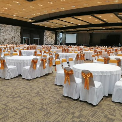 โต๊ะจัดงานกลมพร้อมผ้าคลุมสีขาวและเก้าอี้ผูกโบว์ทองในห้องจัดเลี้ยง