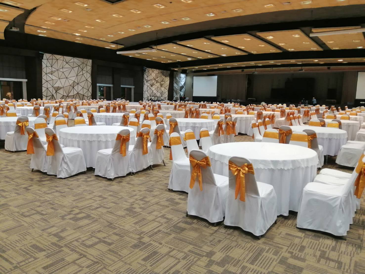 โต๊ะจัดงานกลมพร้อมผ้าคลุมสีขาวและเก้าอี้ผูกโบว์ทองในห้องจัดเลี้ยง