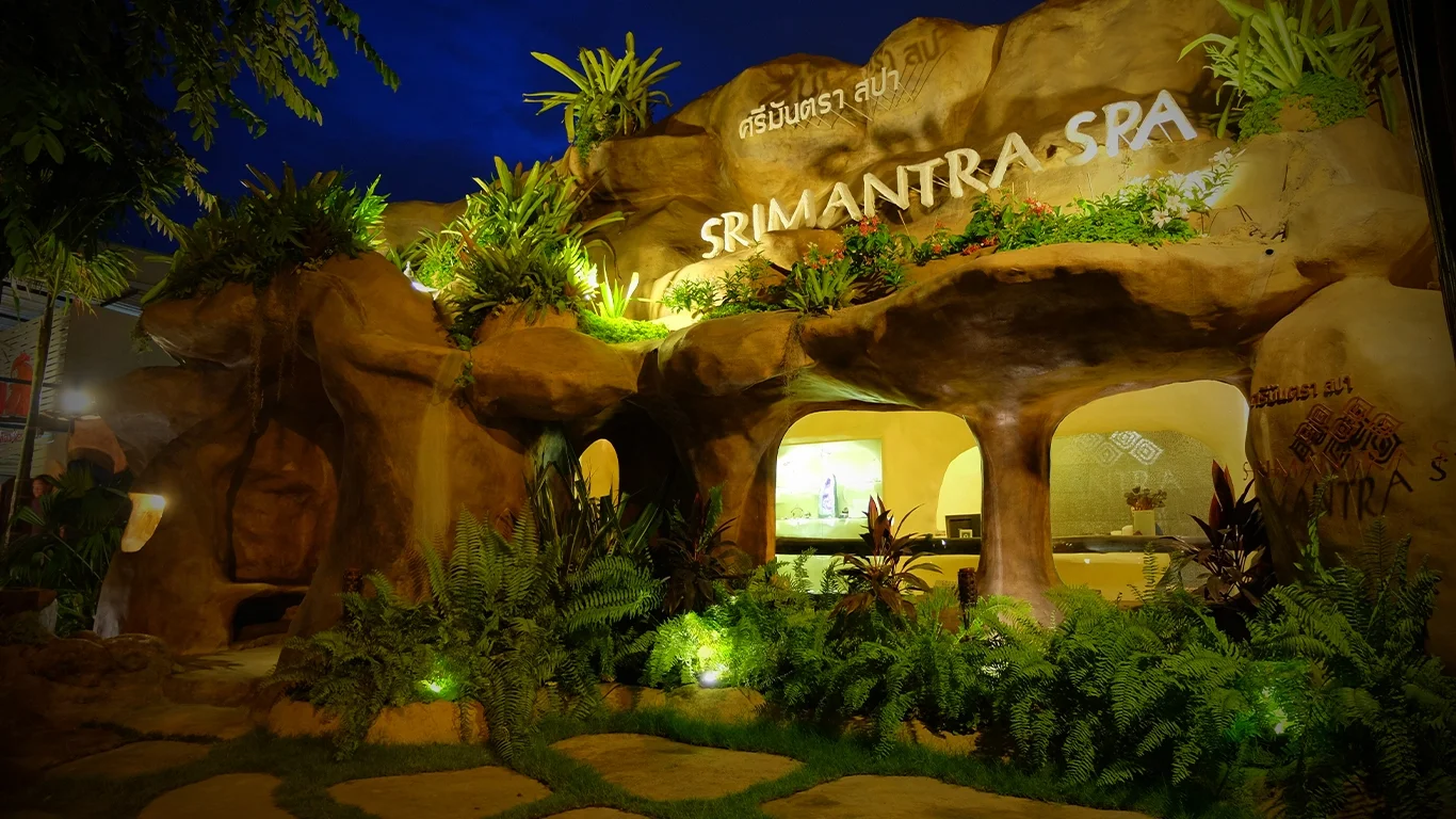 The entrance to Srimantra Spa, adorned with lush greenery and bright lights, creating a relaxing ambiance at night.
