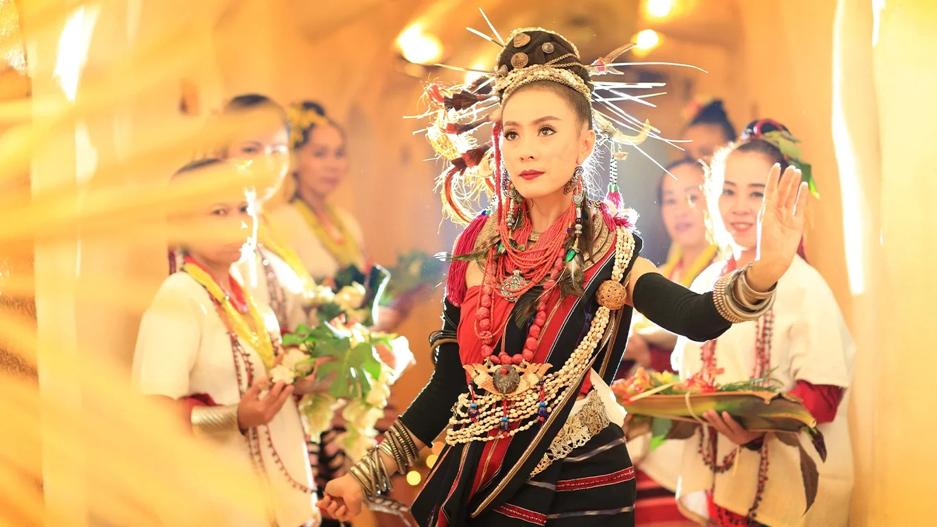 Stunning Lanna performer in traditional attire amidst glowing light, with a group of female performers behind, showcasing Thai culture.