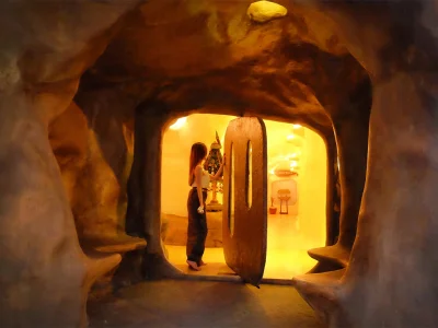 Woman stands before an open wooden door leading into the illuminated cave interior of Srimantra Spa in Chiang Mai, signaling the start of a spa experience.