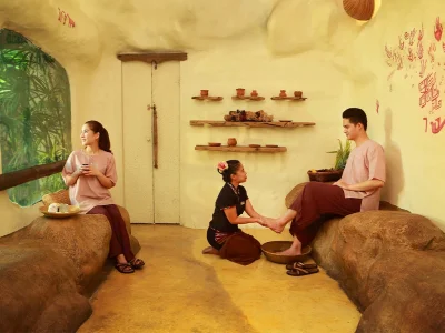Customers receiving foot massages in a cozy, natural cave-like spa in Chiang Mai, decorated warmly with staff in Thai attire.