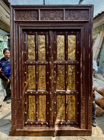 ประตูบานใหญ่ไม้สีเข้มแต่งดอกไม้รอบแผ่นทองเหลือง