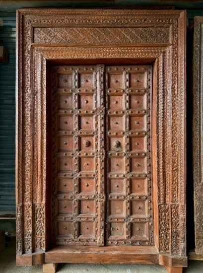 ประตูไม้สักเก่าสีน้ำตาลกลางแกะสลักละเอียดแต่งทองเหลืองดอกไม้